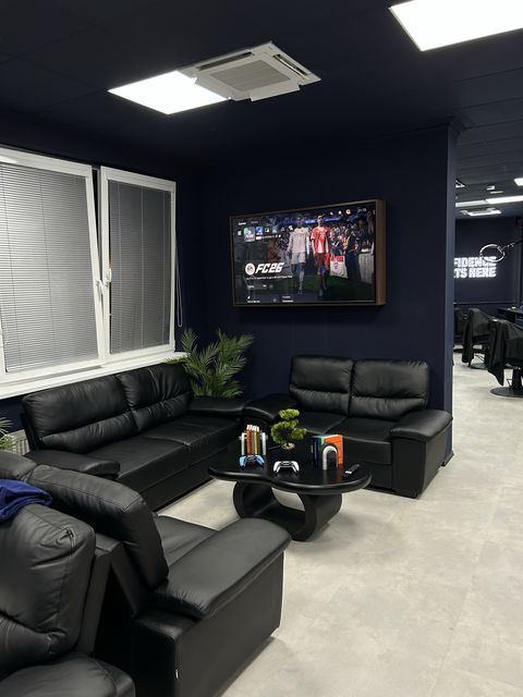 Waiting area with leather sofas and a TV at Barbershop Štýl